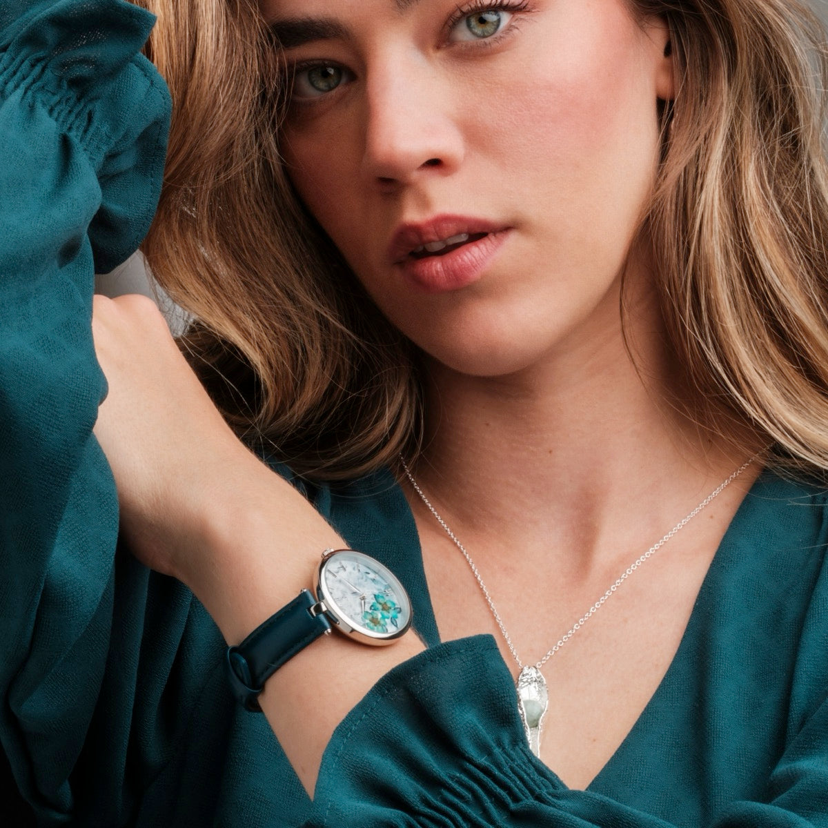 Orologio "Everbloom" con disegno a fiori di prugne e banda blu indossato da una persona in una camicetta teal.