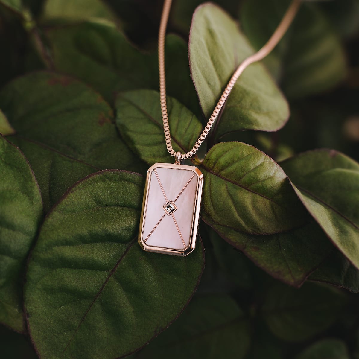 "Collana Aquarell", un elegante collana con accenti in oro rosa e nacre, visualizzati su foglie verdi rigogliose.