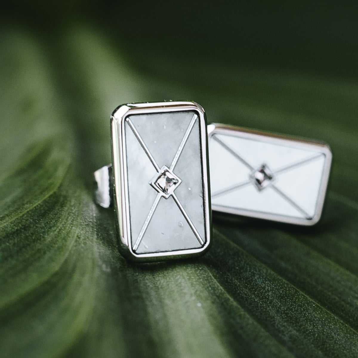 "Aquarell Earrings" earrings feature a modern geometric design with white nacre and silver accents on a leafy background.