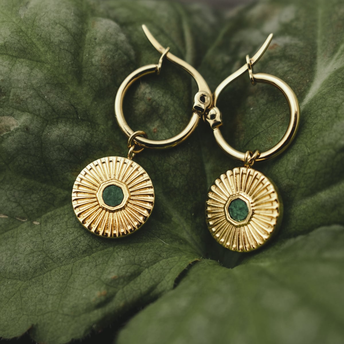 "Stencil Earrings" earrings, featuring a circular design with intricate marble and gold accents, resting on lush green leaves.