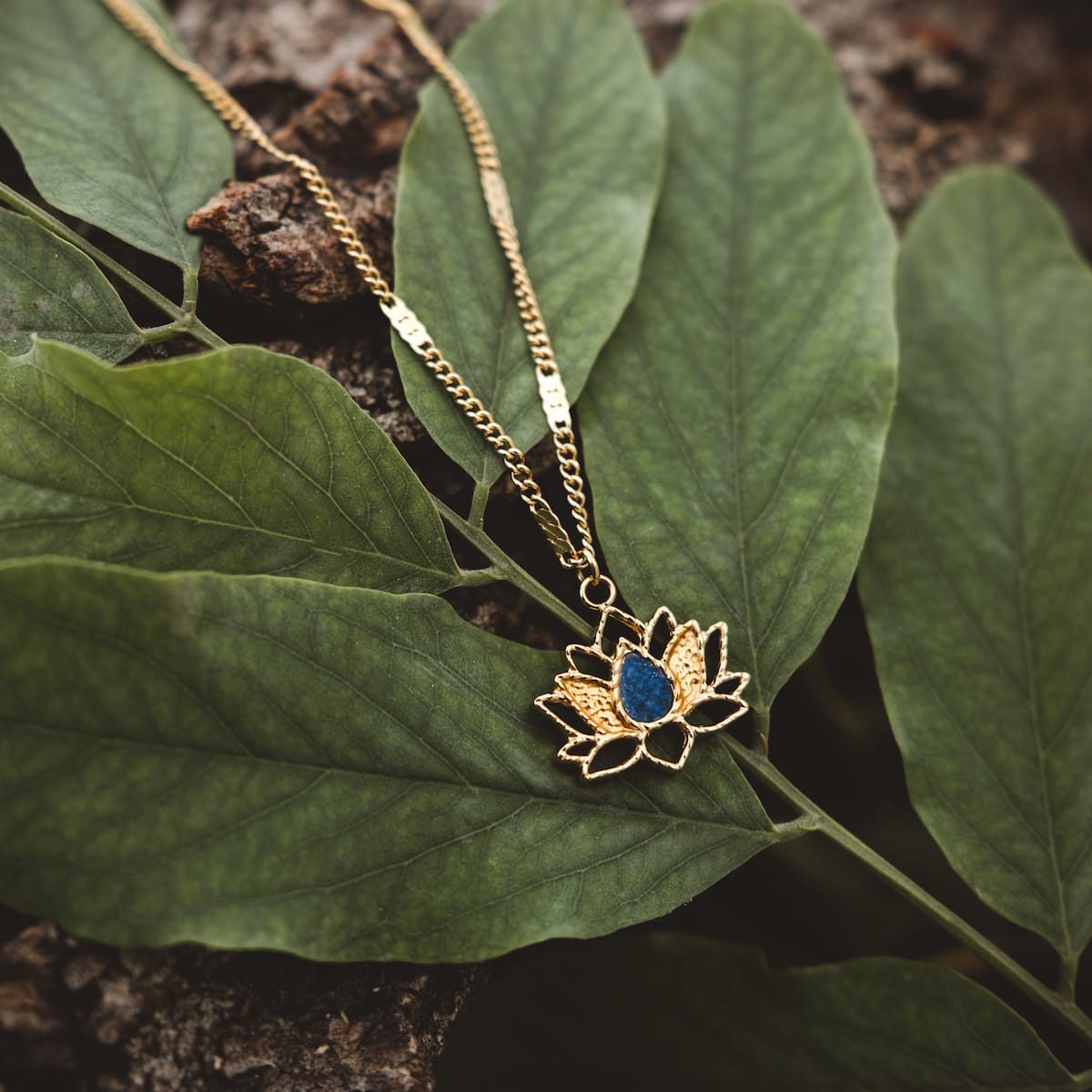 "Collana di danza", una collana d'oro con un ciondolo Lapis Lazuli, mostrata su fondo fogliare.