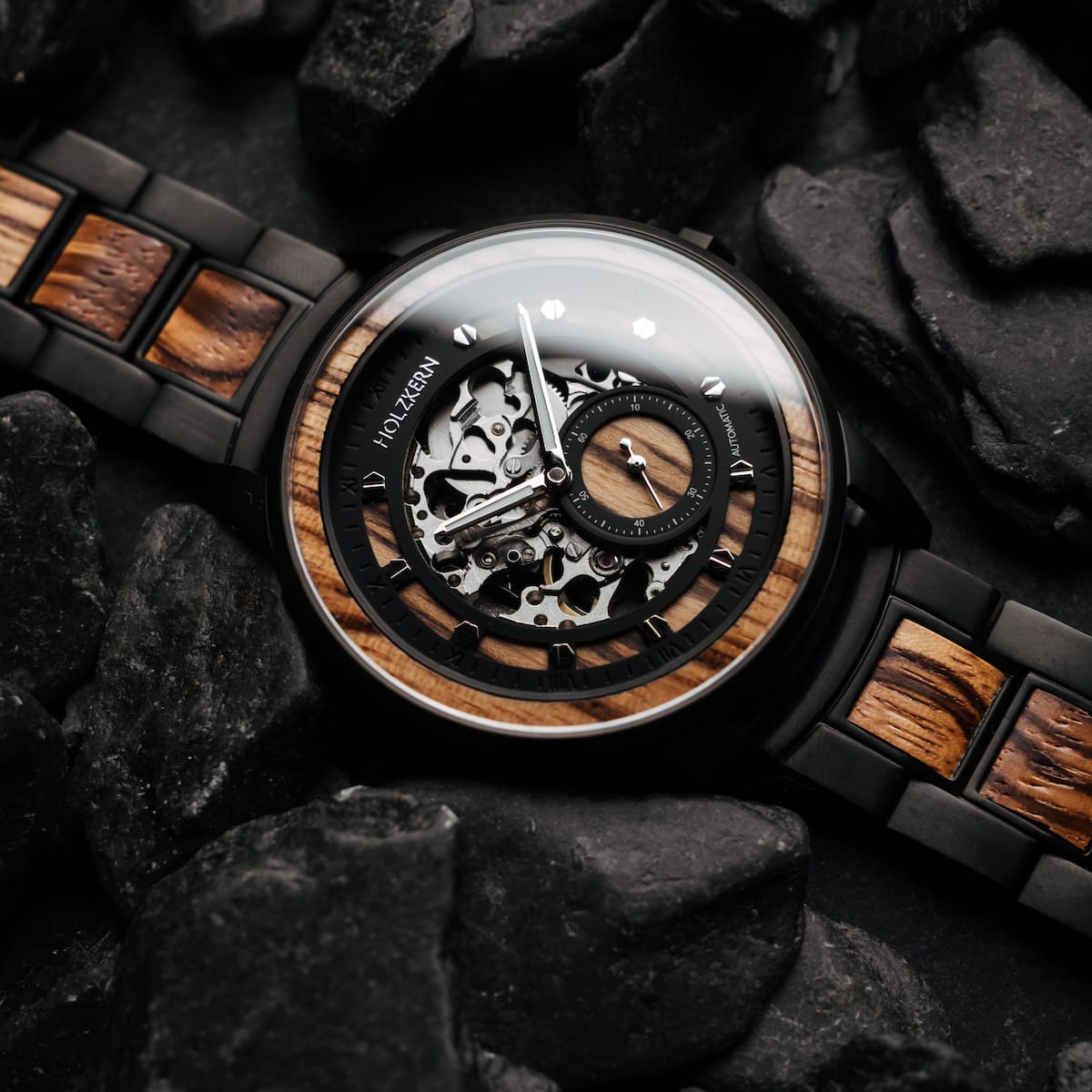 L'orologio "Sternum" presenta un sorprendente zebrawood e un design nero con meccanica a vista, impostato contro pietra scura.
