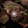 "Composition Gem Bracelet", a stylish bracelet featuring a moonstone centerpiece and rose gold accents, set against lush leaves.