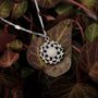 "Composition Gem Necklace" necklace in silver with a moonstone gem, featuring an intricate floral design on a leafy background.