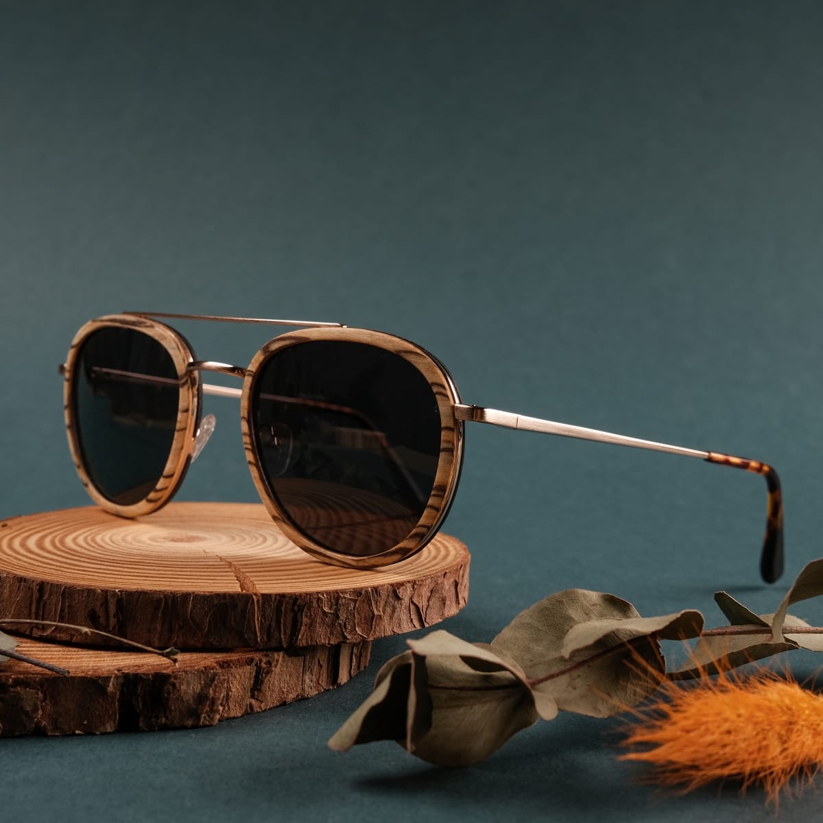 Occhiali da sole "The Risky" con cornici in zebrawood e accenti in oro opaco, presentati su una superficie in legno rustico.