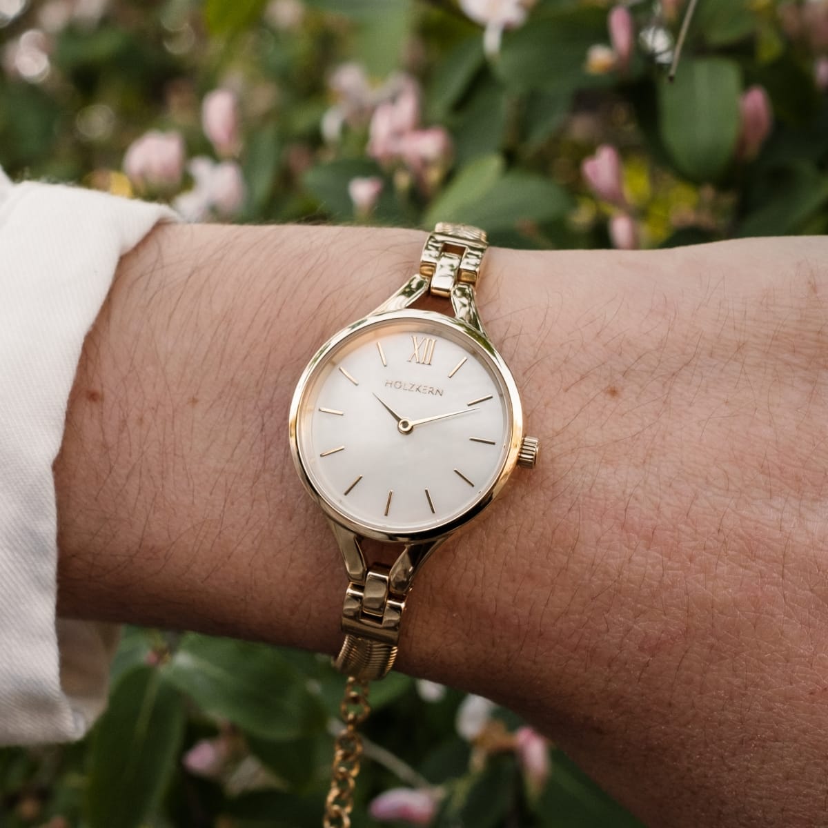 Elegante orologio "Kaliya" con un viso nacre e bracciale in oro, impostato su uno sfondo floreale.