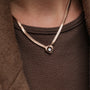 Collana "Awakening Collana", con un design in oro rosa e grigio, indossato sopra un top marrone con texture.