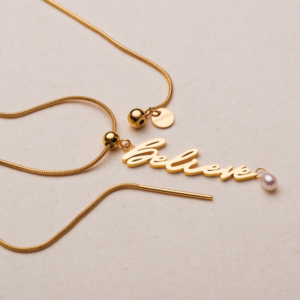 "Believe-Charm" necklace in gold with pearl accent, featuring a stylish script charm design.