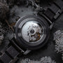 Orologio da polso in carbonio con finitura acero grigio scuro e design meccanico intricato.