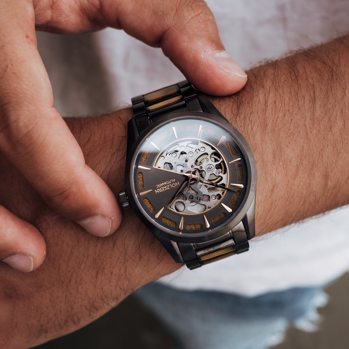 "Tenoumer" watch with a koa wood and dark grey design, featuring an open-face dial and metal wristband.