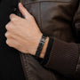 Bracciale "Tremolo", elegante metallo grigio scuro sinistro, indossato con una giacca di pelle casual.