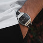 "Kéré", un elegante orologio da polso dal design elegante, caratterizzato da un quadrante nero e bracciale in metallo con accenti acero.