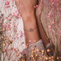 "Aphonia Bracciale", un delicato bracciale, presenta un design intricato in tonalità di oro e rosa su uno sfondo floreale naturale.