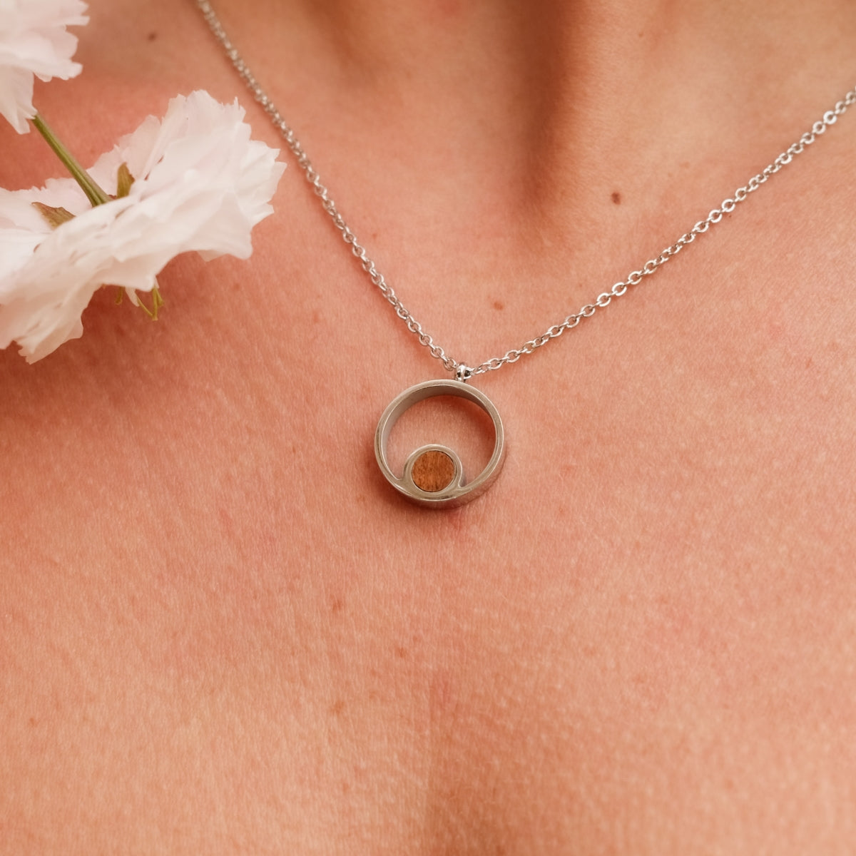 Collana "Pigment Collana" con un design circolare con accenti in legno di koa e argento, indossato elegantemente contro la pelle.