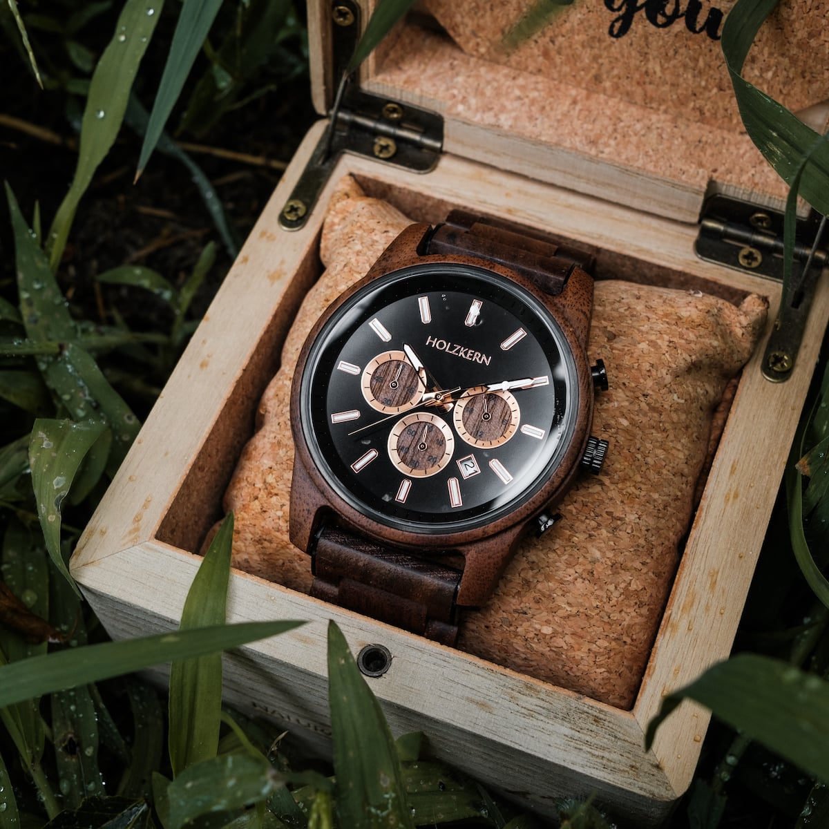 "Thicket" watch with walnut and marble accents, nestled in a rustic wooden box amidst lush greenery.