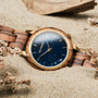 "Balos" watch featuring Zebrawood and Marble with an elegant design style on sandy background.
