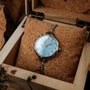 Orologio "Brighter" in finitura nacre e argento, con un design elegante con quadrante azzurro, presentato in una scatola di legno.