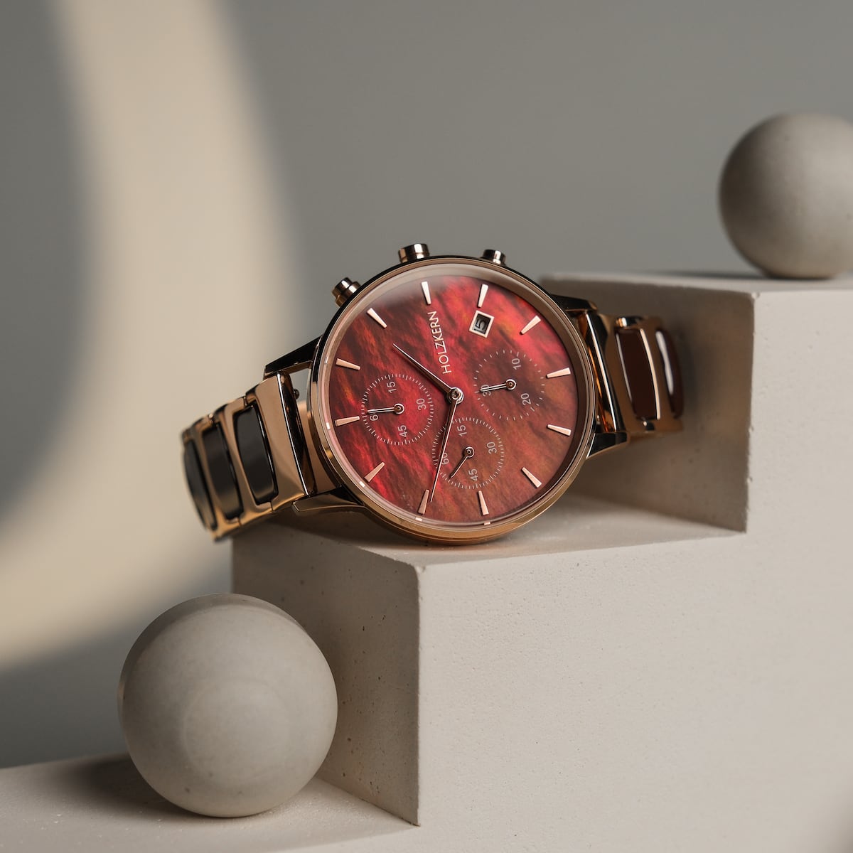 "Cheery", un orologio elegante con un quadrante rosso e accenti in ceramica, elegantemente esposto su una superficie geometrica.