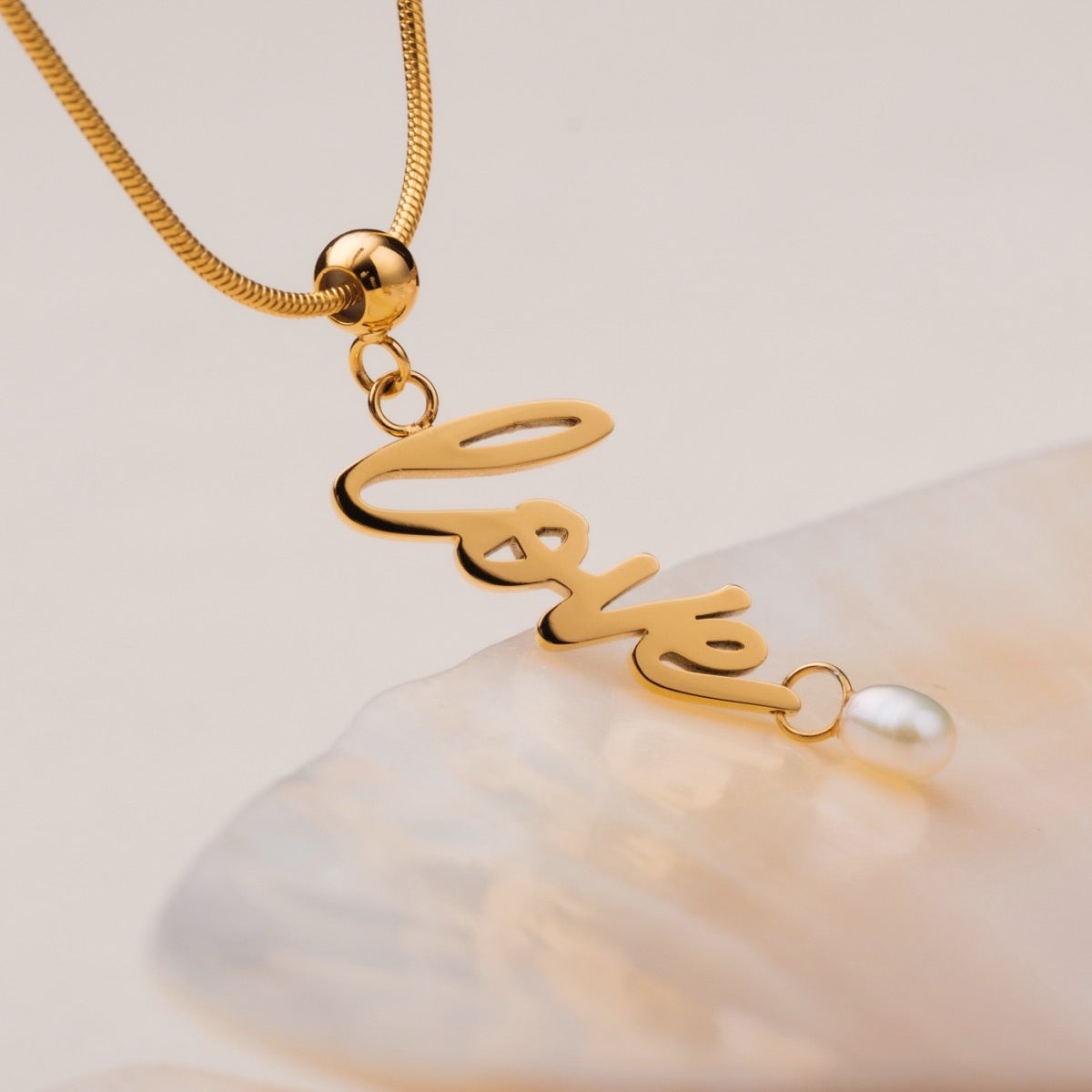 La collana "Love-Charm" presenta un elegante script in oro con un accento perla, che mostra un design affascinante e sofisticato.
