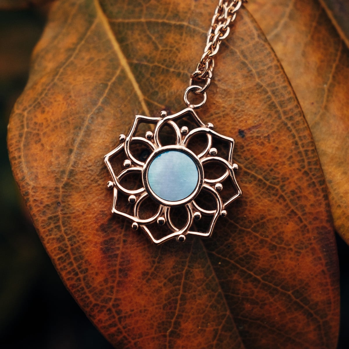 "Composition Necklace", a rose gold necklace, features a delicate blue nacre design with intricate detailing.