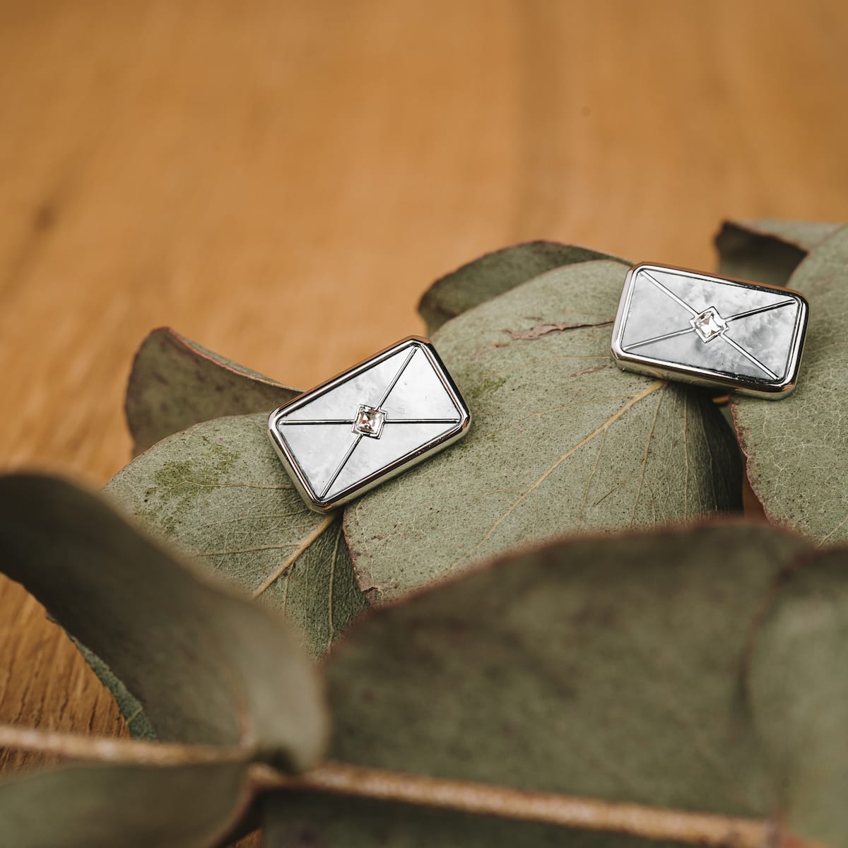 "Aquarell Earrings" earrings with a white nacre and silver design, displayed on greenery.