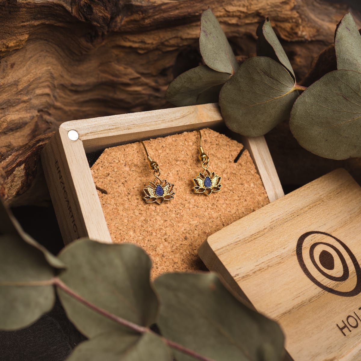 "Balance Earrings", elegant earrings with Lapis Lazuli and gold accents, showcased in a wooden box with natural elements.
