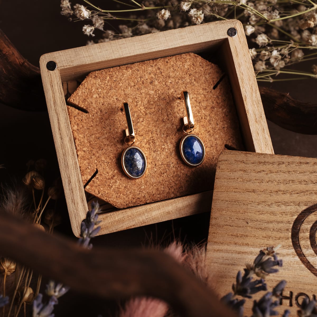 Orecchini a specchio: Eleganti orecchini con lapis lazuli e accenti d'oro, presentati in una scatola di legno rustico.