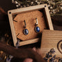 Orecchini a specchio: Eleganti orecchini con lapis lazuli e accenti d'oro, presentati in una scatola di legno rustico.