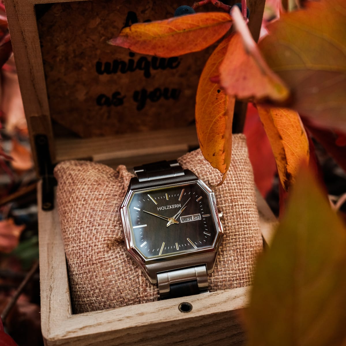 Orologio "Kéré" con accenti acero, visualizzato in una scatola di legno rustico con foglie di autunno.