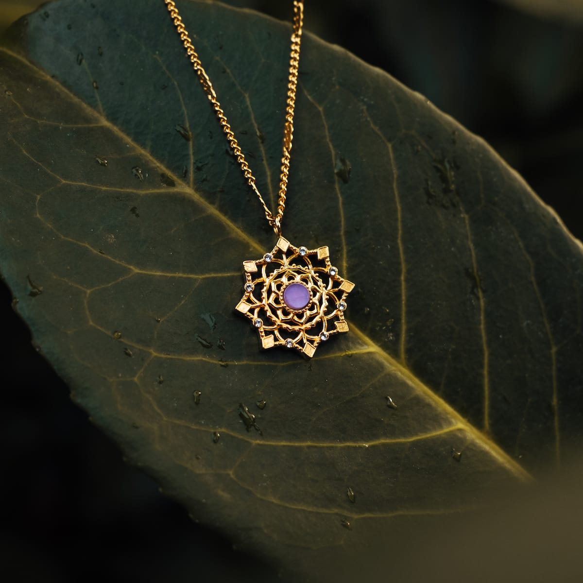 "Aphonia Necklace": Elegant gold necklace with amethyst centerpiece, featuring intricate design on a leafy background.