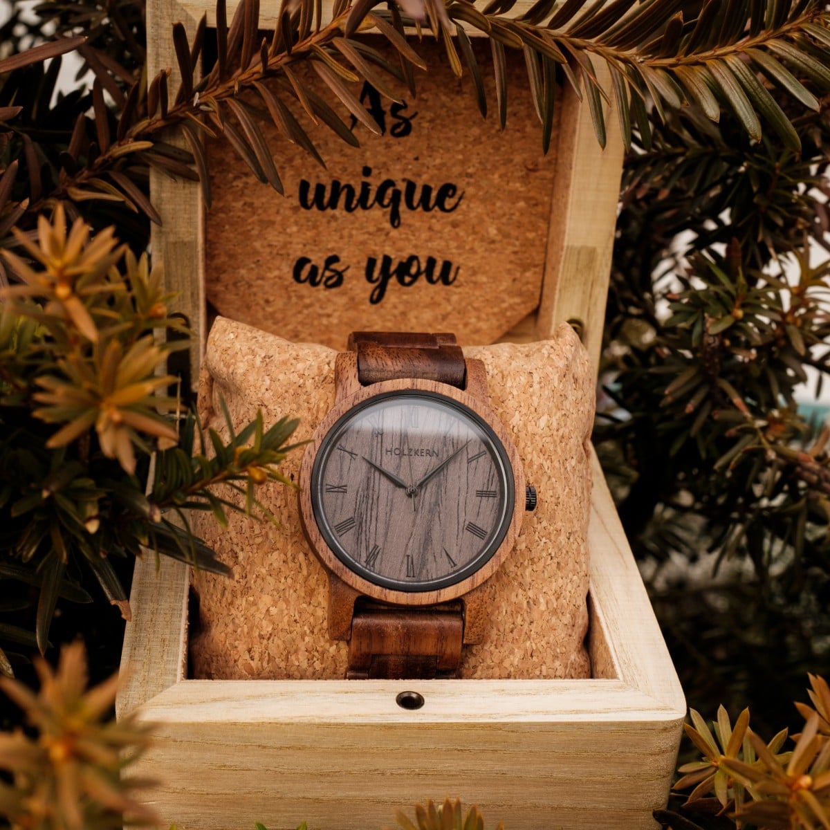 Orologio "Spring Evening" in noce e legno di piombo, ambientato in una scatola di legno rustica circondata da fogliame.