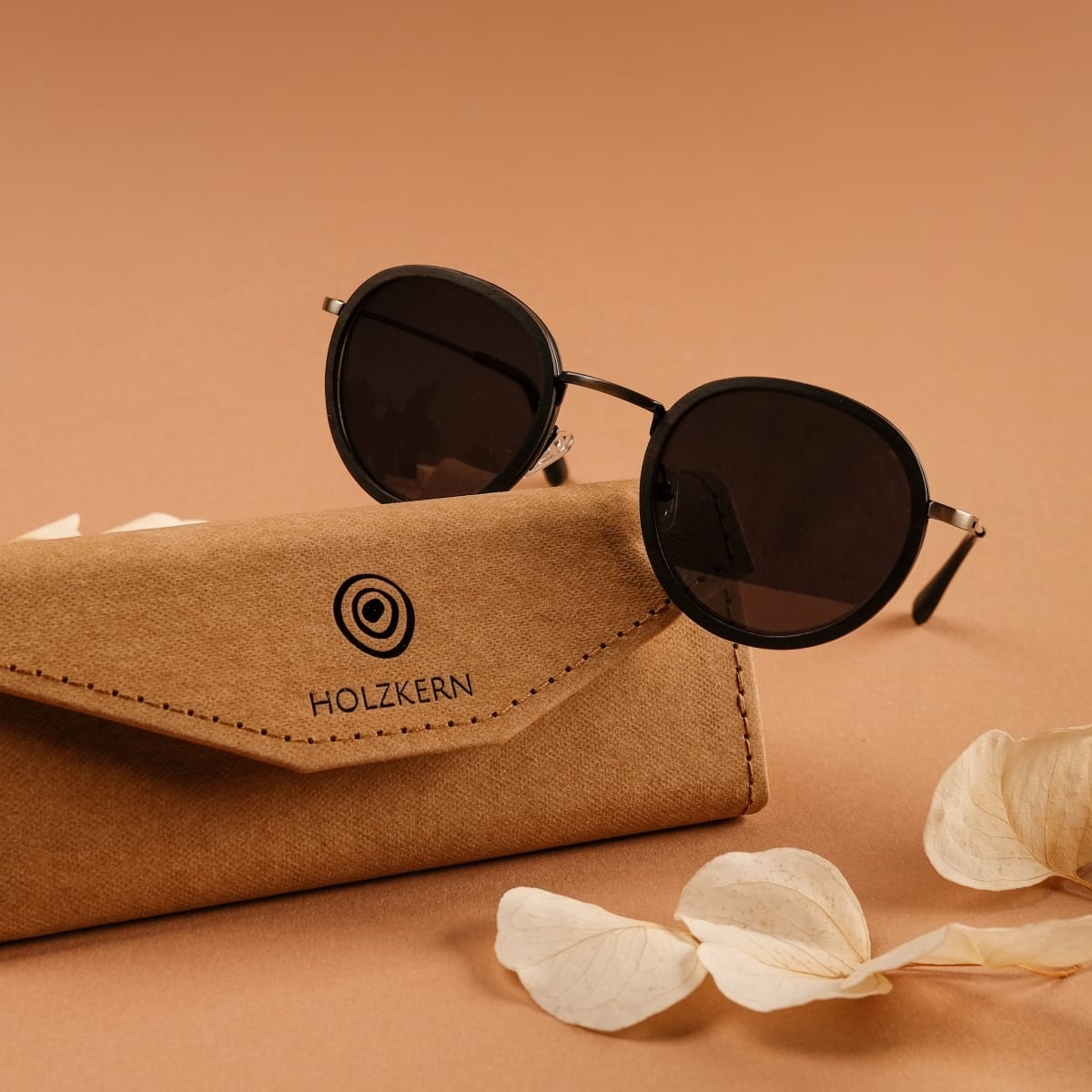 "The Radiant S" sunglasses in Leadwood/Dark Grey style, featuring a sleek, modern design with a brown case.