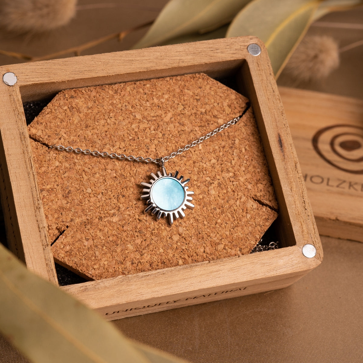 "Shade Necklace" necklace featuring a blue nacre center in a silver sunburst design, presented in a wooden box.