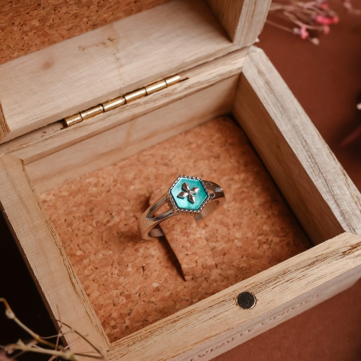 "Spectral Ring", un anello in argento con intarsio nacre, visualizzato in una scatola di legno rustico.