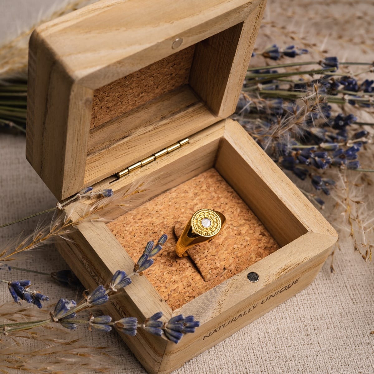 Anello "Pixa Ring" con centro bianco in oro, elegantemente presentato in una scatola di legno rustico.