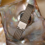 "Piccolo" watch with a nacre and silver finish, featuring a stylish mesh band displayed on an iridescent background.