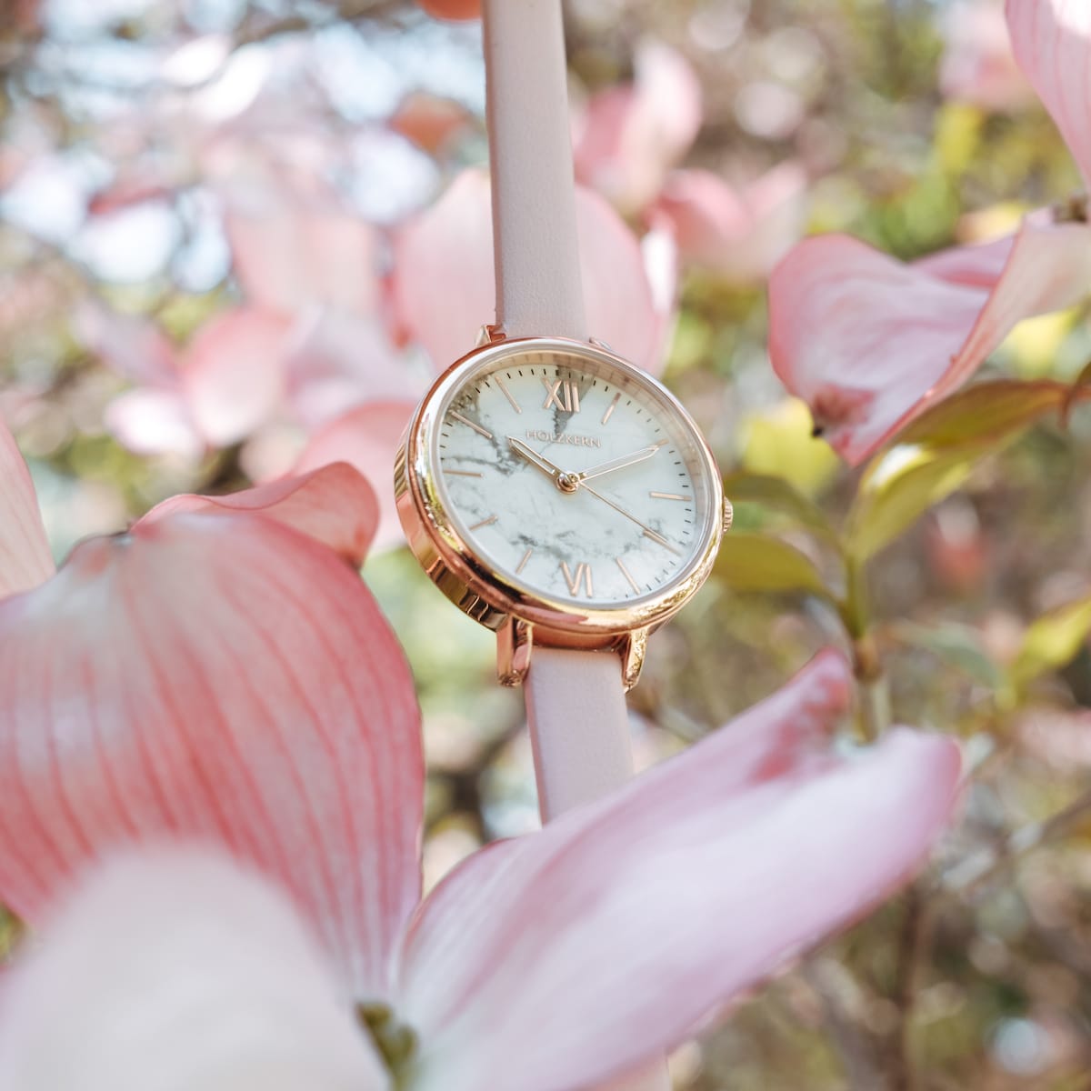 "Alva" watch, featuring a marble face with rose gold accents, set against a floral background.