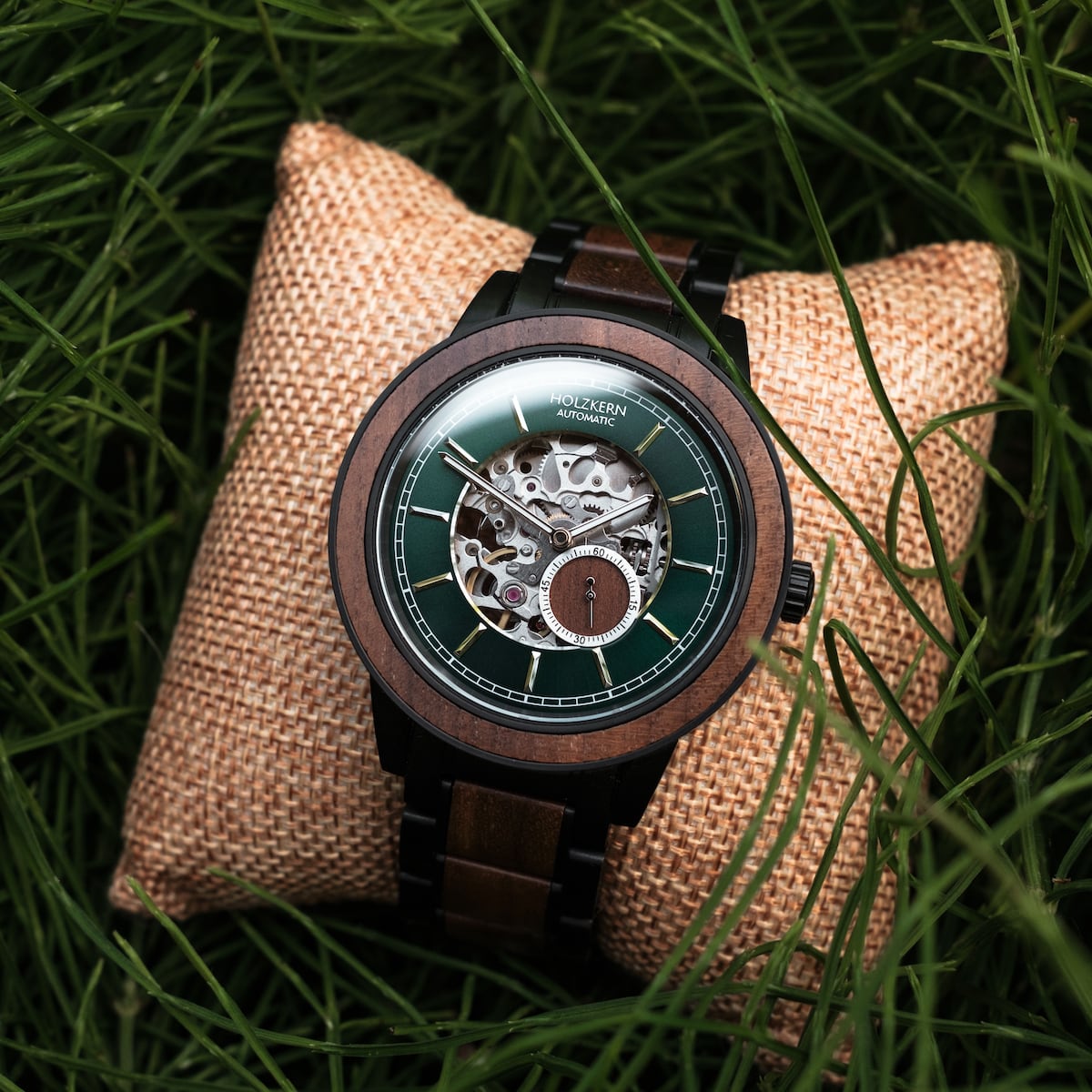 Orologio "Sigiriya", con un design in noce con un quadrante verde su un cuscino rustico circondato da erba.