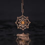 Collana "Aphonia Collana", caratterizzata da un design intricato in oro e oliva rosa, elegantemente sospesa su uno sfondo scuro.