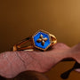 Anello "Spectral Ring" con un design blu nacre e oro che poggia elegantemente su uno sfondo foglia.