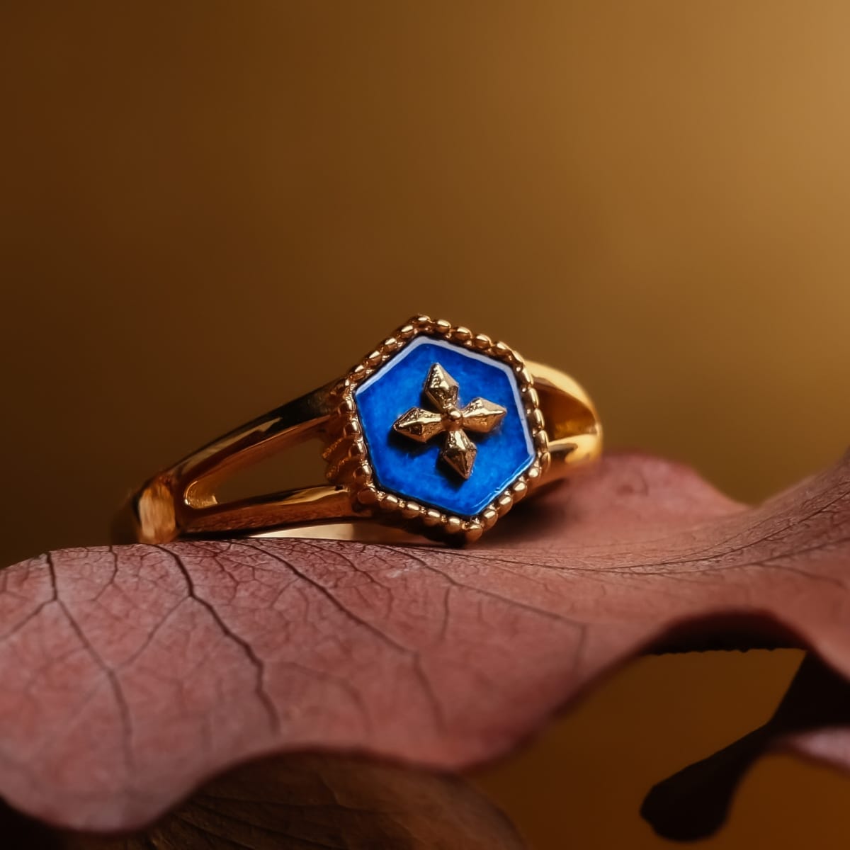 Anello "Spectral Ring" con un design blu nacre e oro che poggia elegantemente su uno sfondo foglia.