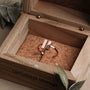 "Campania Ring": a stylish ring in walnut and rose gold with a minimalist design, displayed in a rustic wooden box.