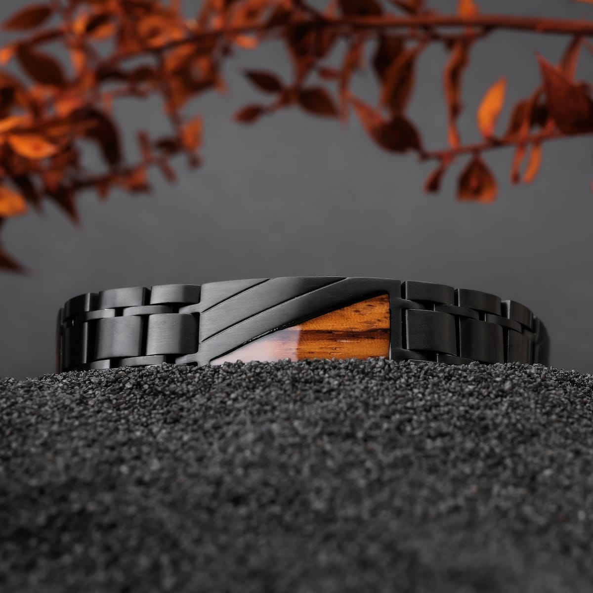 "Looper", un braccialetto elegante in zebrawood e metallo nero, poggia su una superficie nera con texture con foglie autunnali.