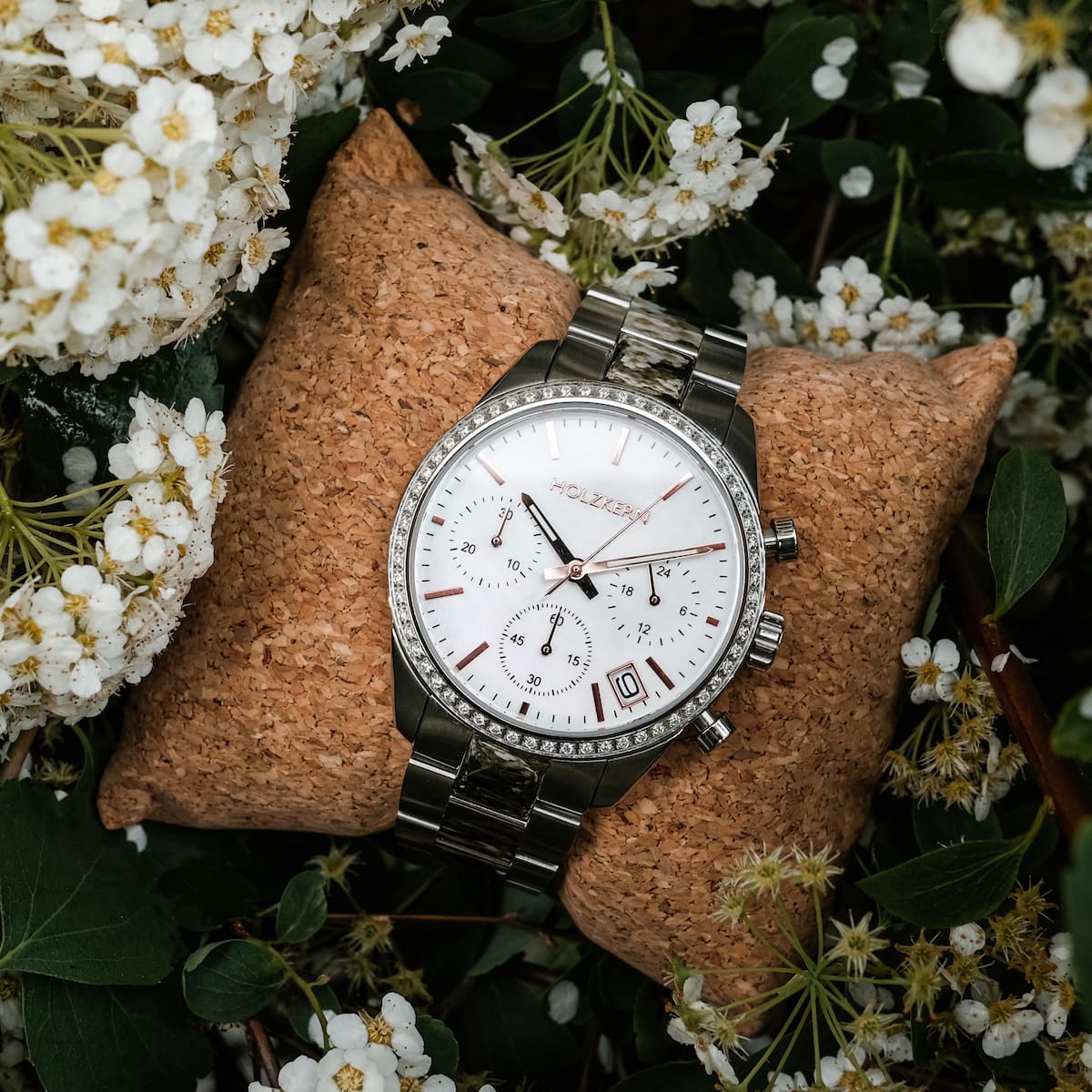 "The Balanced", un elegante orologio da polso con elementi in argento e in bianco, elegantemente esposto tra delicati fiori bianchi.