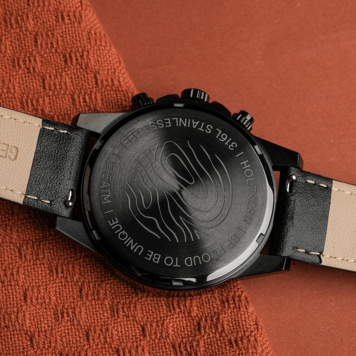 "Rackets watch featuring a sleek, black design and intricate detailing on the back, laid on a textured orange surface."