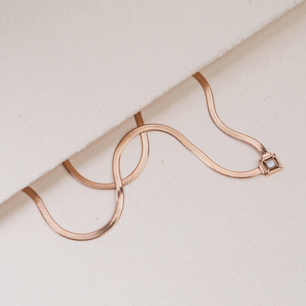 "Collana in attesa", una collana in oro rosa con un elegante accento nacre, sdraiata su una superficie bianca morbida.