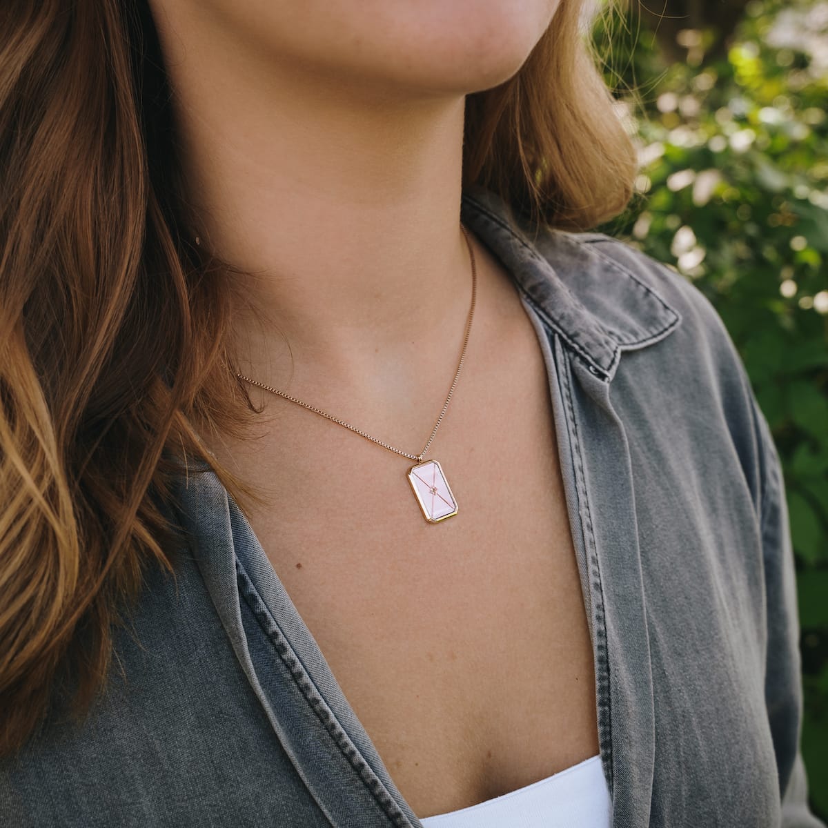 "Collana Aquarell", un elegante collana con un design in oro rosa e grigio, indossato da una persona all'aperto in un outfit casual.