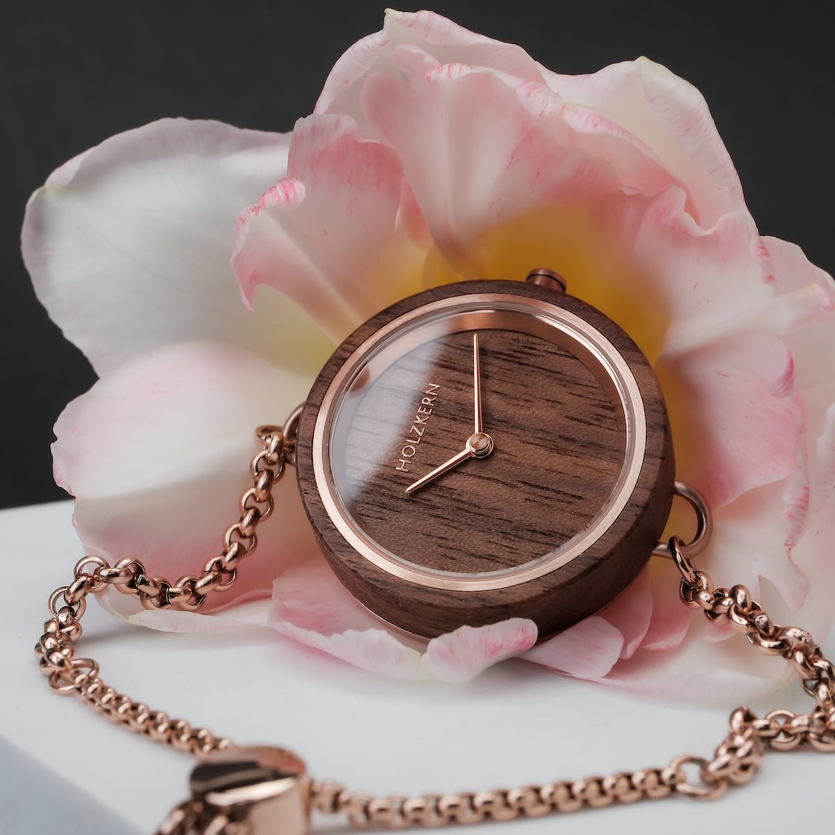 Orologio "Leave" con finitura Walnut e accenti in oro rosa, ambientato su un morbido sfondo di fiori rosa.