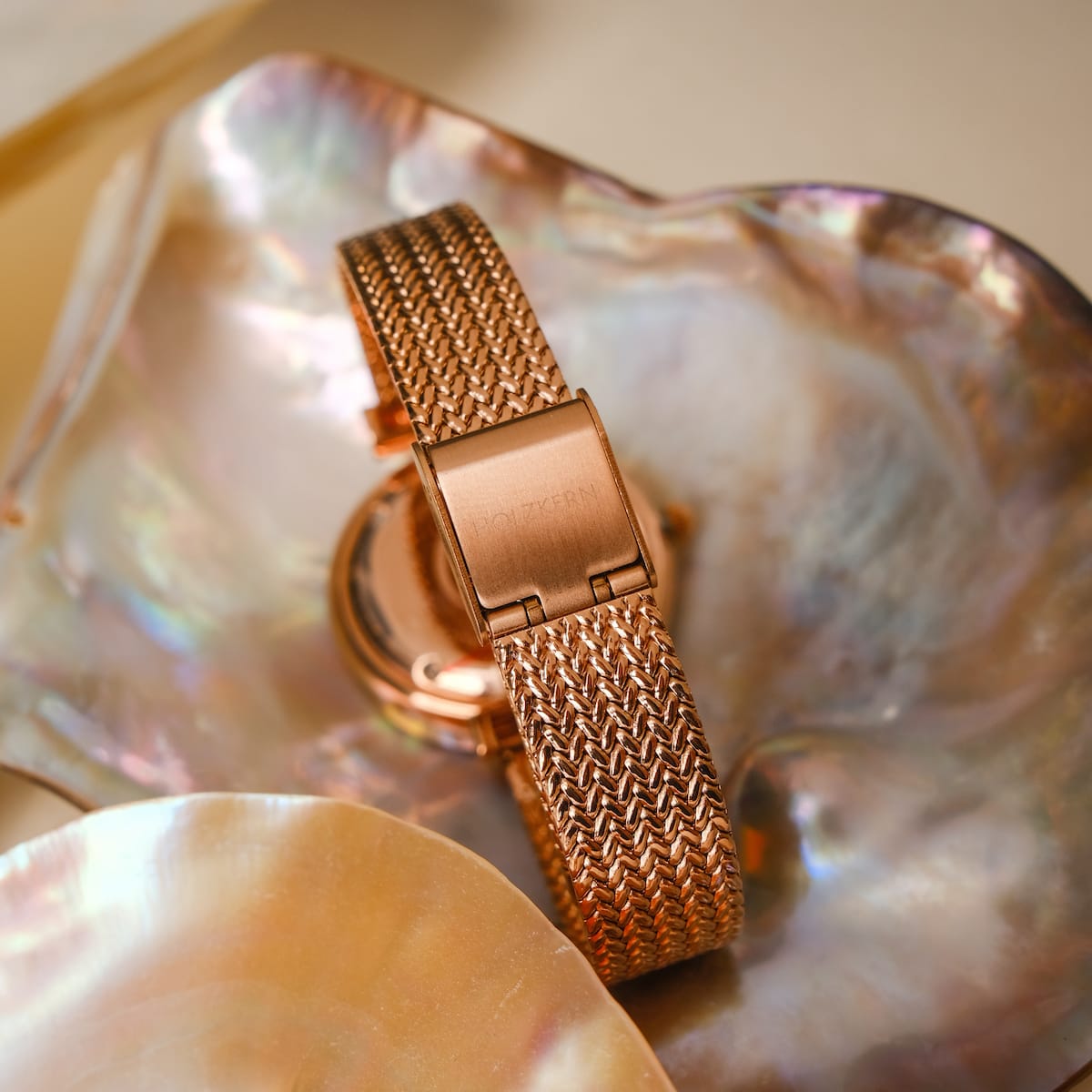 Orologio "Chitchat" con una fascia in mesh oro rosa su uno sfondo nacre.