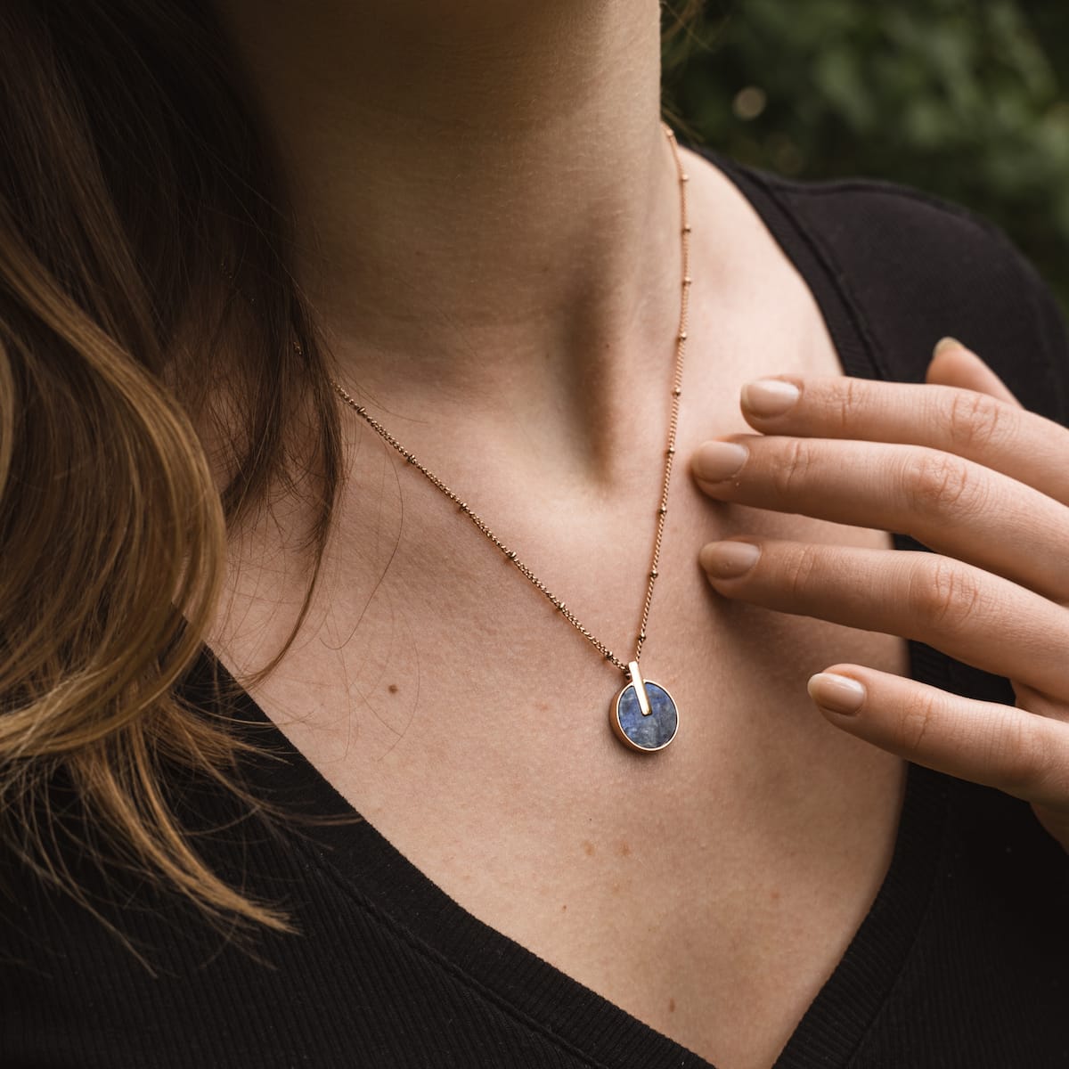 "Opacity Necklace": A stylish necklace featuring a blue marble pendant with rose gold accents, worn on a delicate chain.